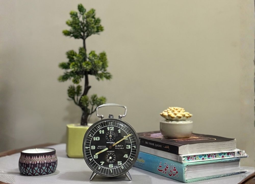 Books, candle, small plant, and alarm clock on a table representing preparation for Friday Sunnahs